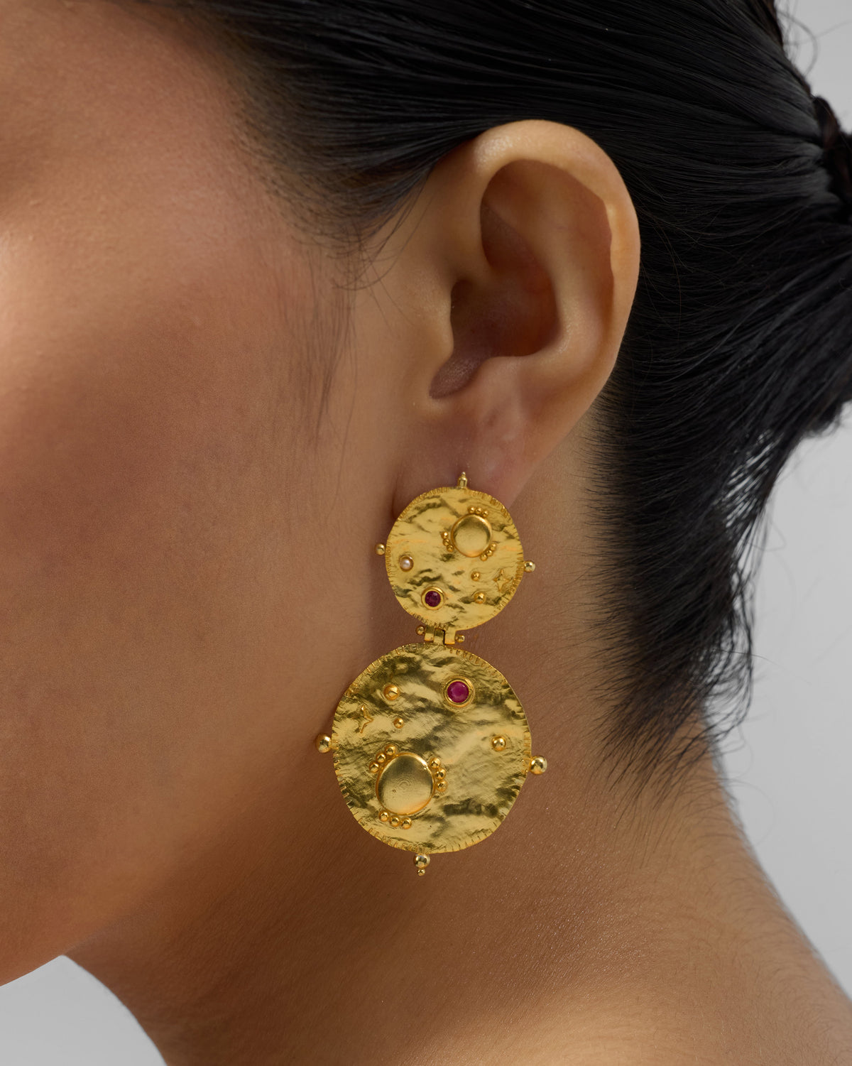 Side profile of gold Rishi disc drop earrings on a person.