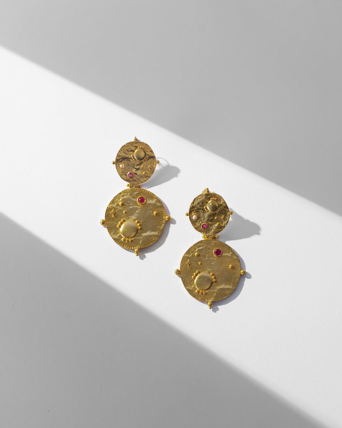 Pair of gold Rishi disc drop earrings laid flat.