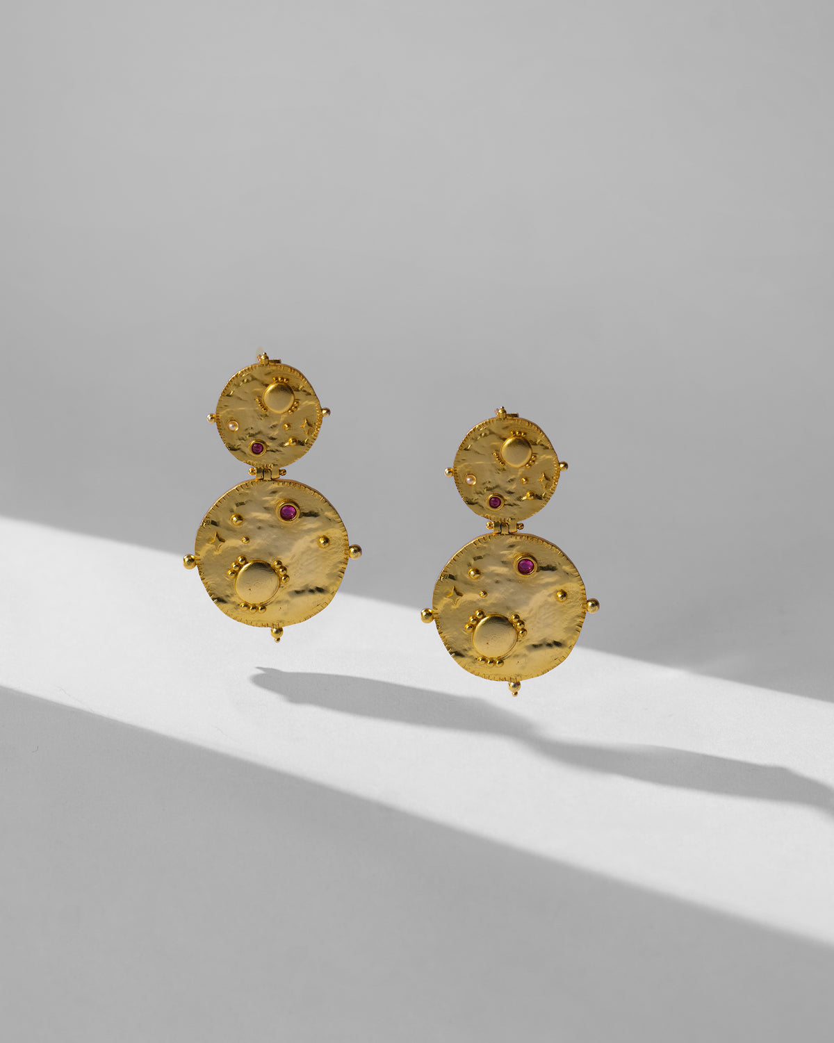 Pair of gold Rishi earrings with hammered discs and red stones.