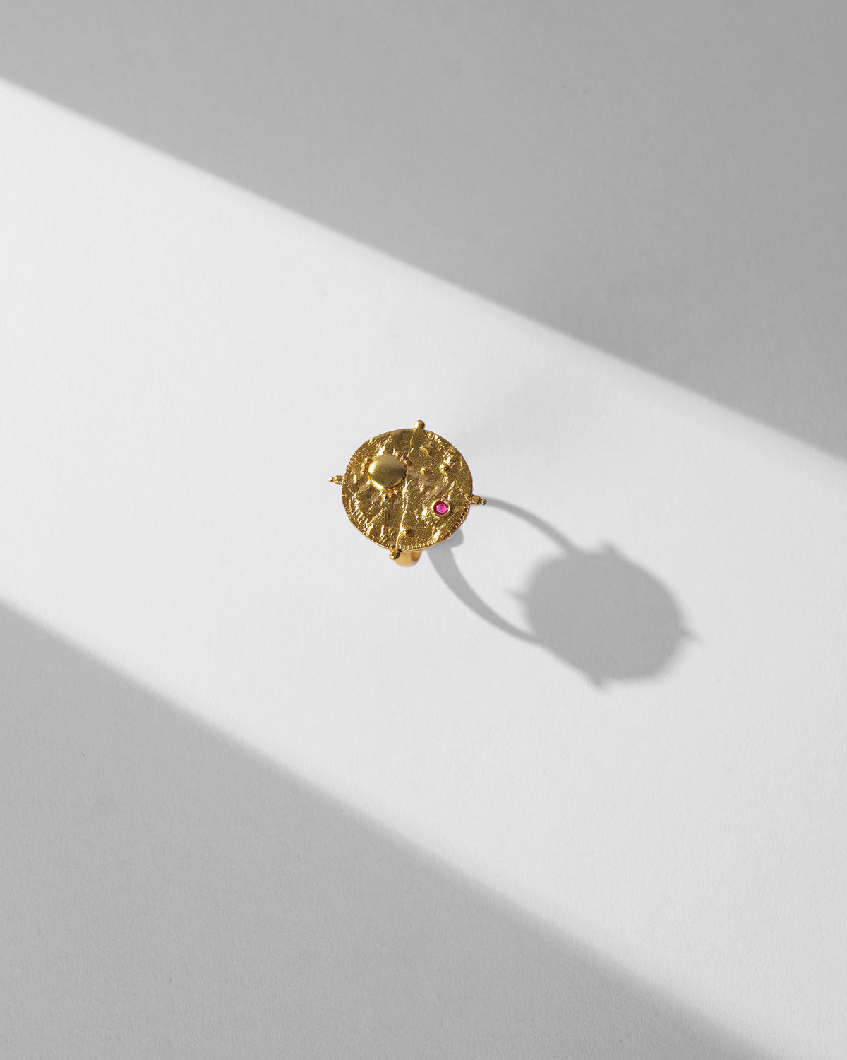 Gold Nebra ring with a textured disc face and pink stone.