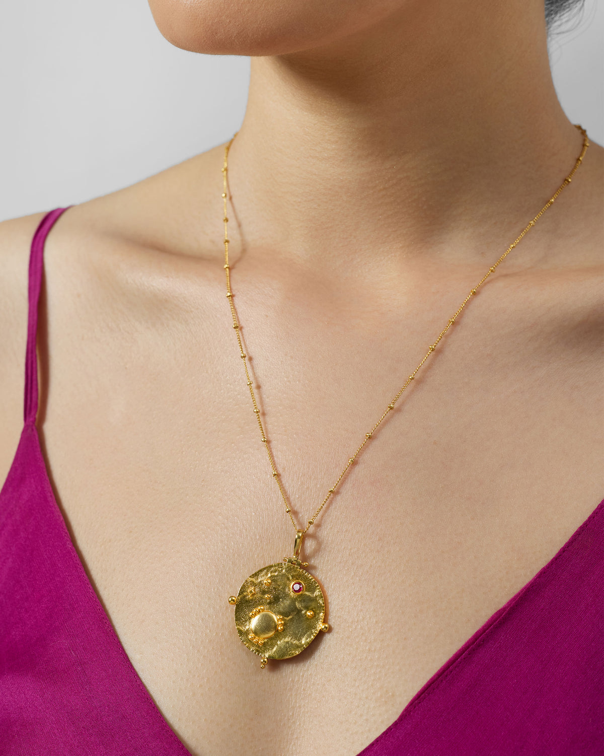 Gold Nebra necklace with textured round pendant and red stone worn at the chest.
