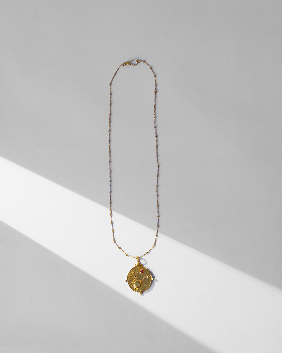 Gold Nebra necklace laid flat with a textured medallion and red stone.