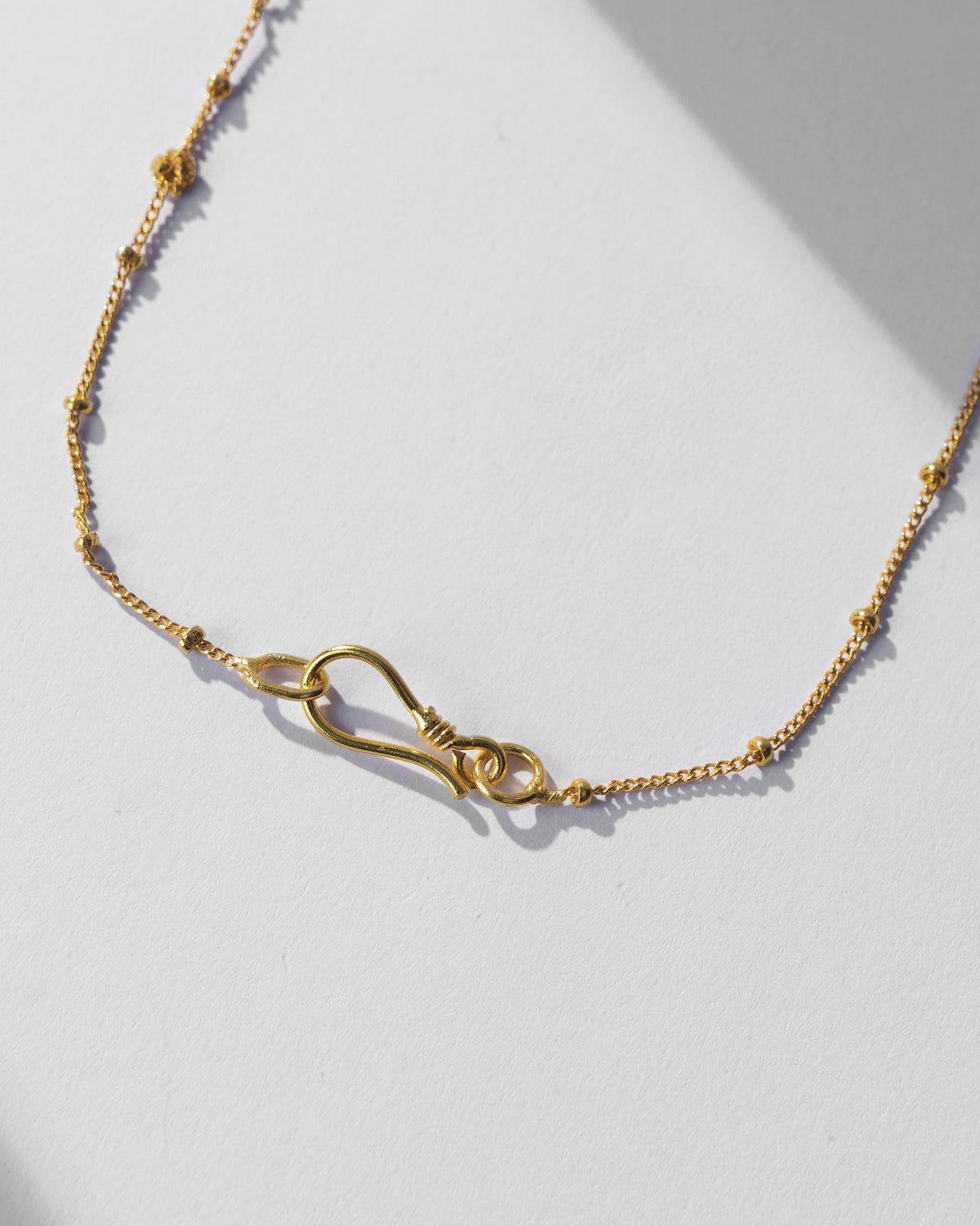 Close-up of the gold Nebra necklace satellite chain and S-hook clasp.