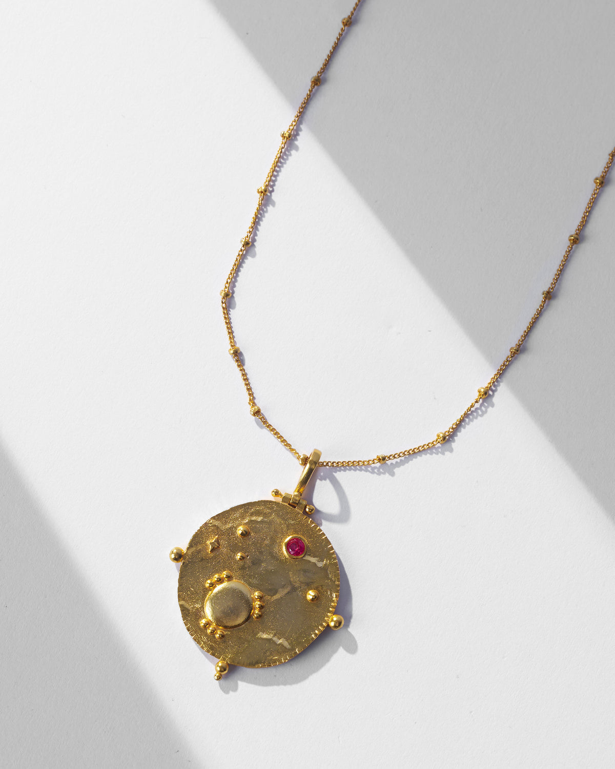 Close-up of Nebra necklace medallion with hammered gold and a red stone.