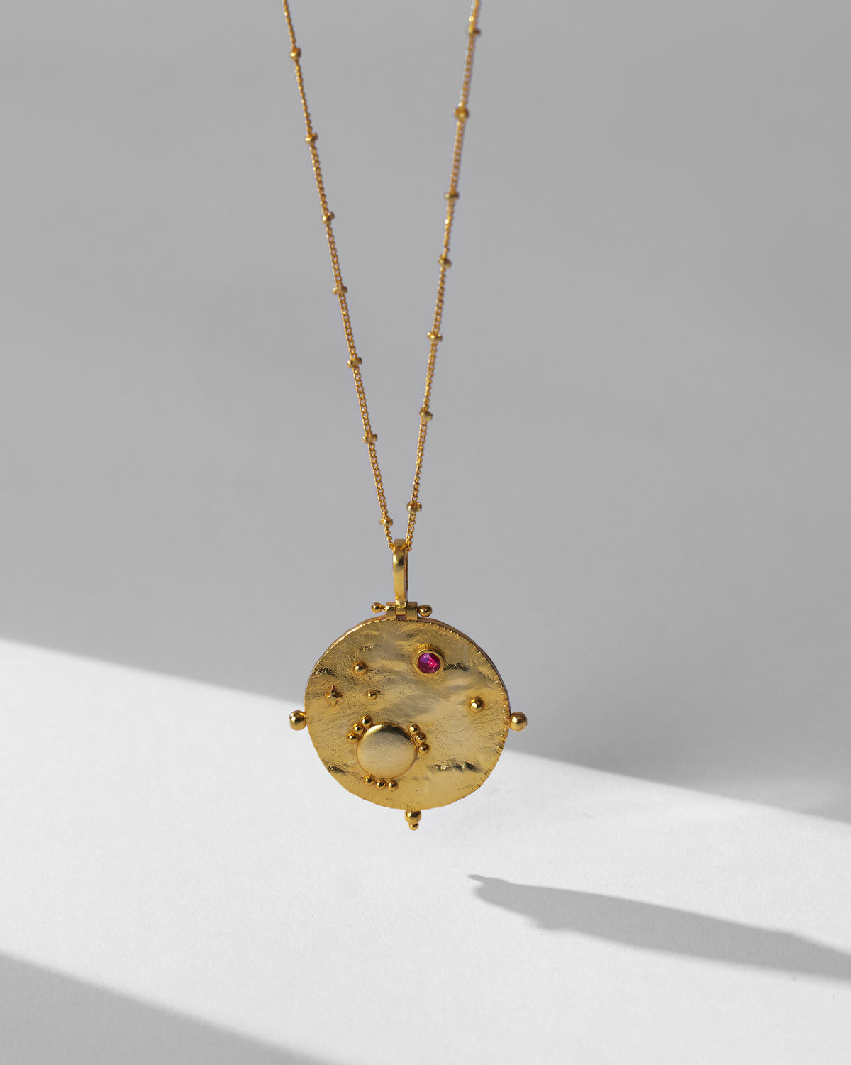 Gold Nebra necklace hanging to show the textured medallion and red stone.
