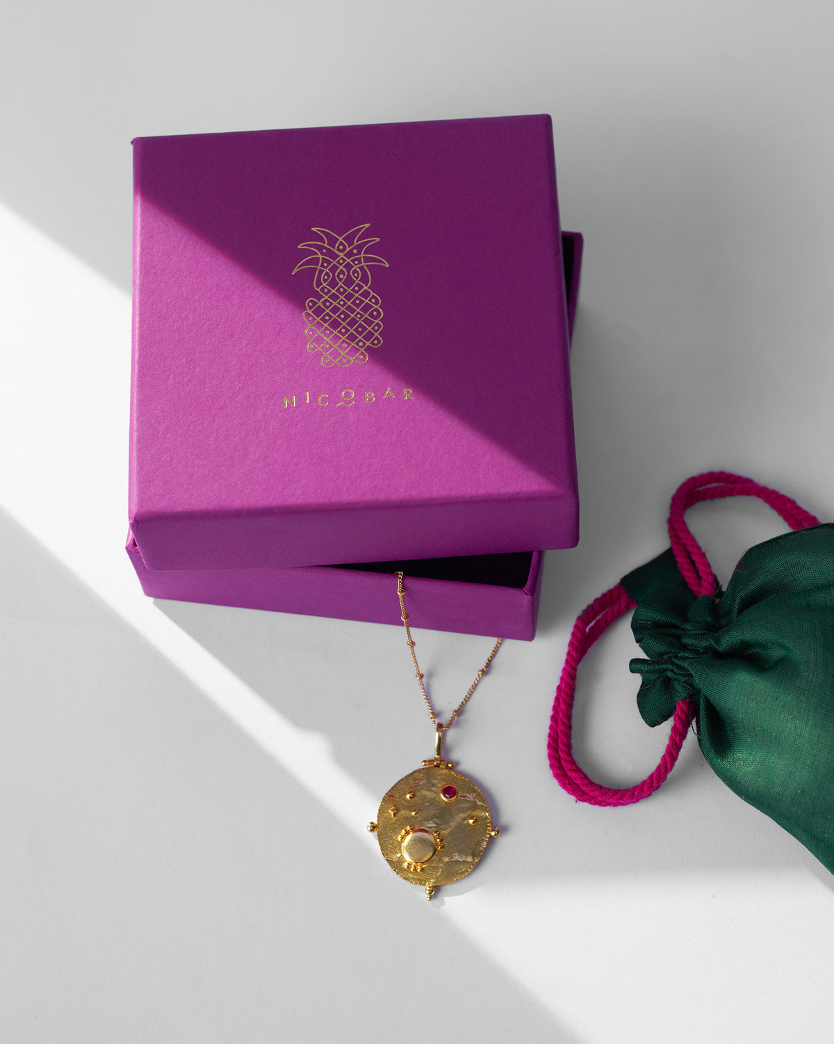 Gold Nebra necklace with magenta Nicobar gift box and green pouch.