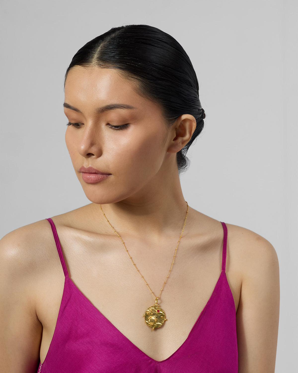 Person wearing a gold Nebra necklace with a textured round pendant.