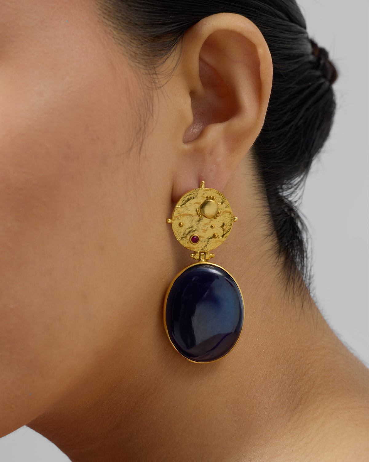 Side profile of a gold Nebra earring with a navy glass drop.