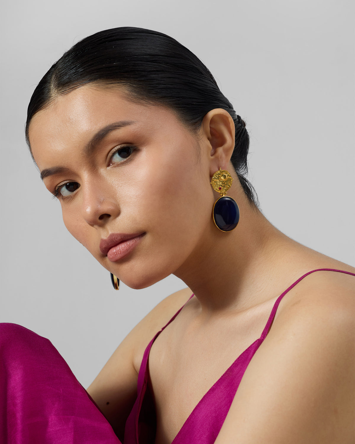 Person wearing gold Nebra earrings with navy glass drops.