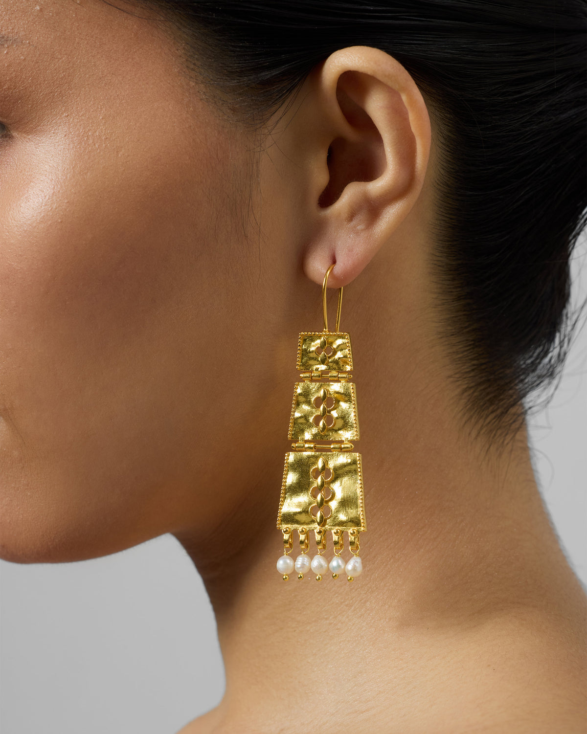 Side profile of long gold column earrings with pearl fringe.