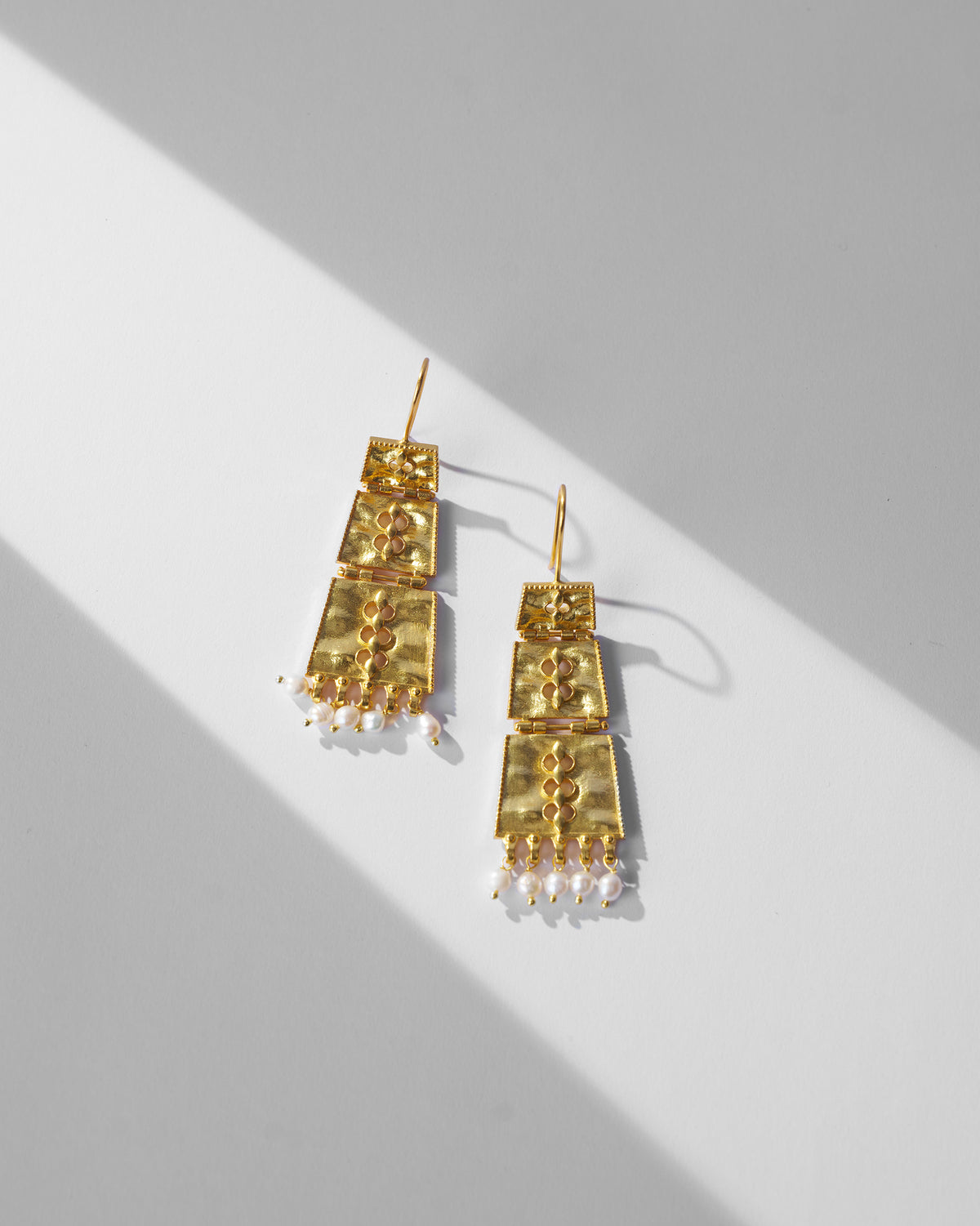 Pair of gold column earrings with pearl drops laid flat.
