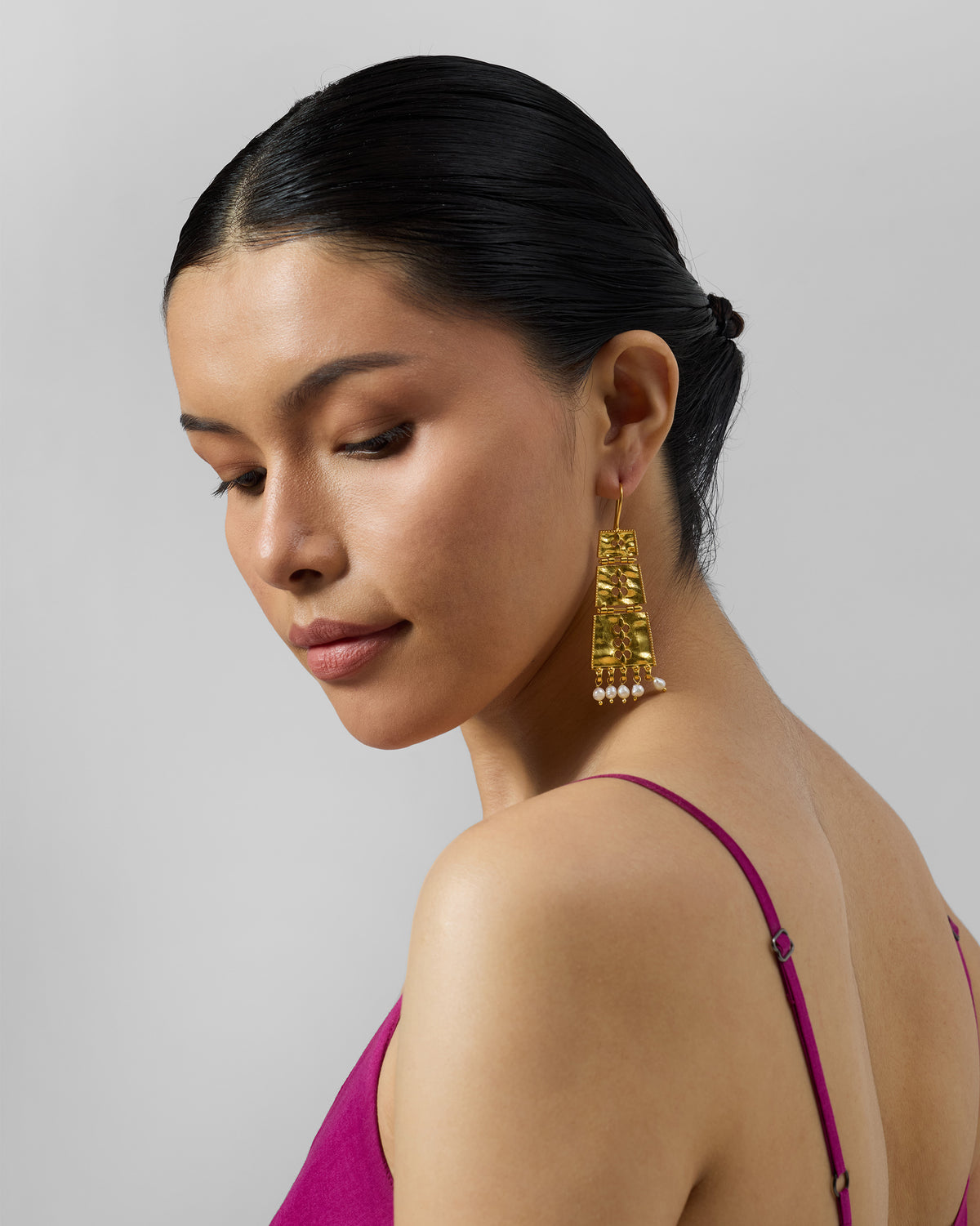 Person wearing a long gold column earring with pearl fringe.