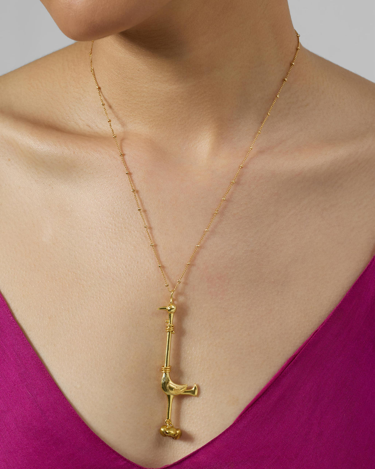 Gold Saras necklace with a long bird pendant worn at the chest.
