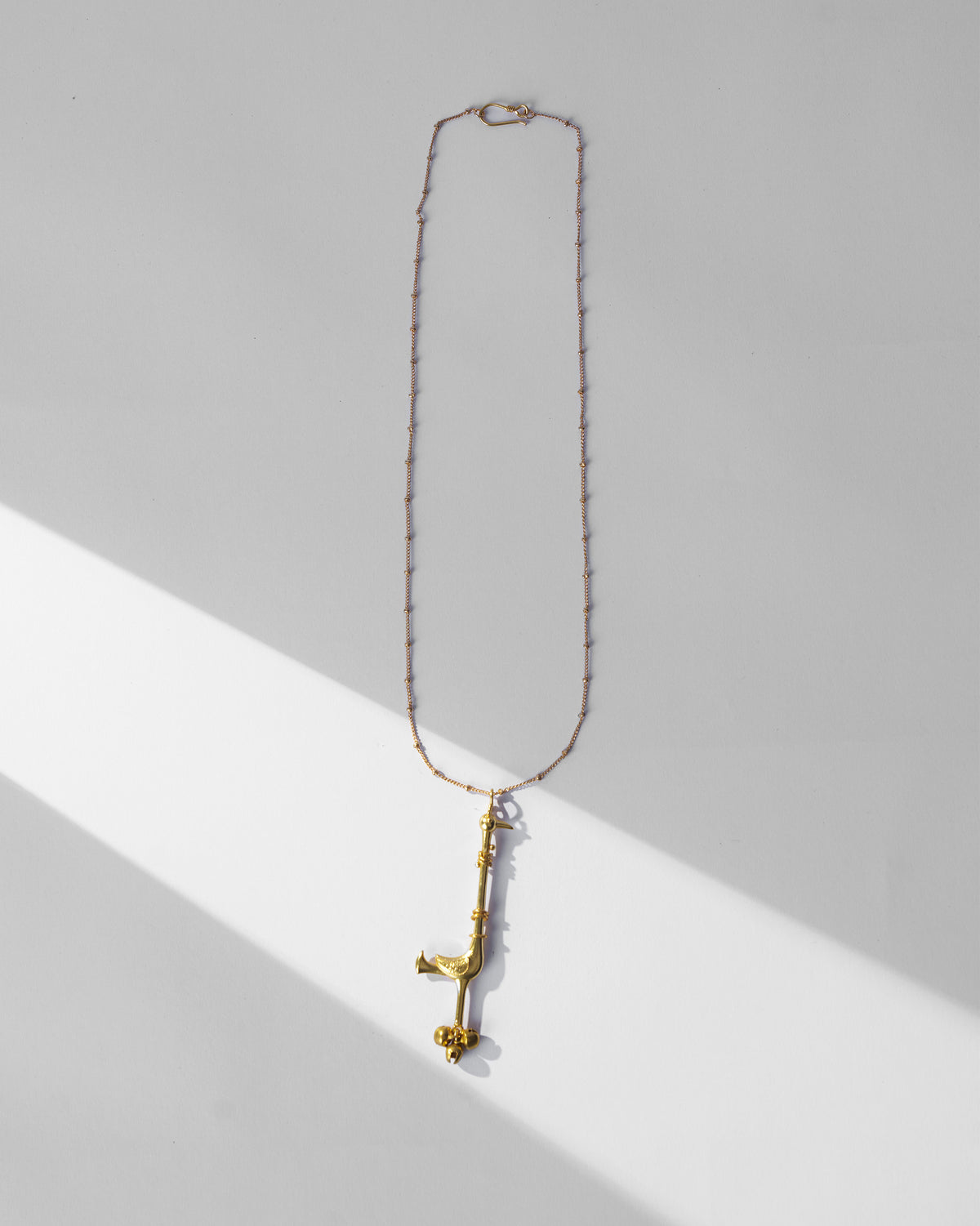 Gold Saras necklace laid flat with a slender long-necked bird pendant.
