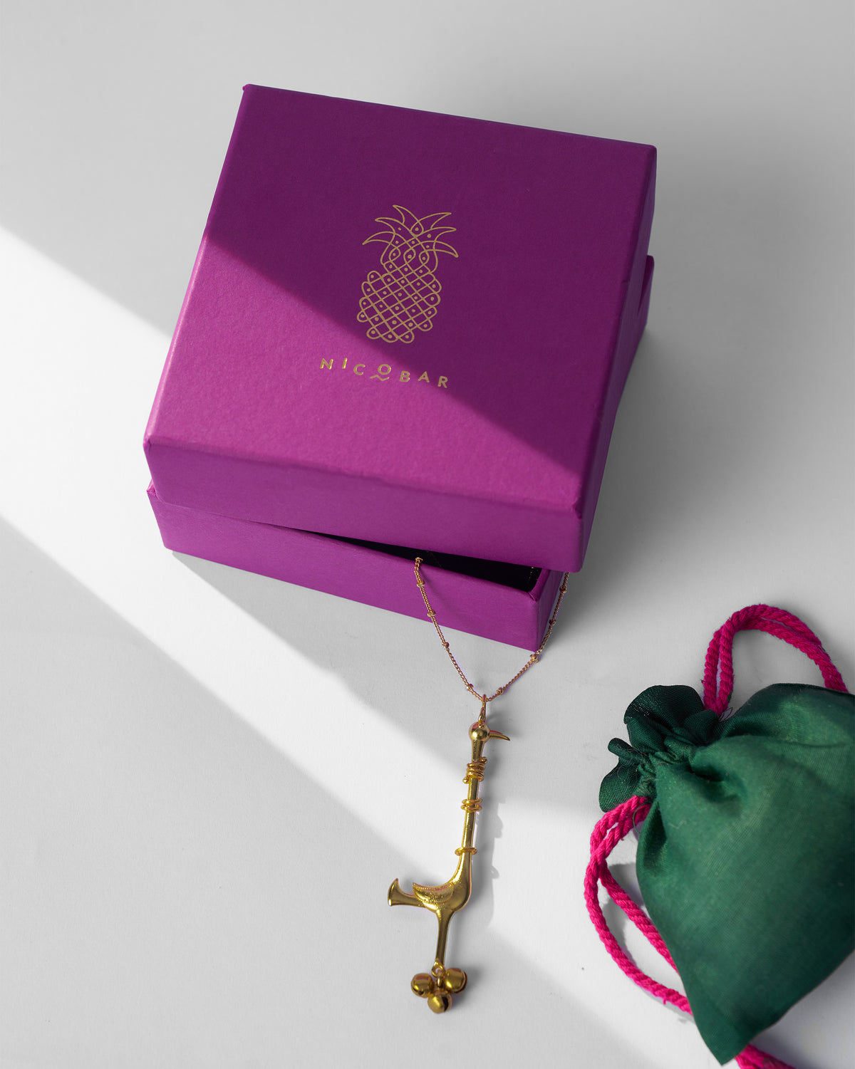 Gold Saras necklace with magenta Nicobar gift box and green pouch.