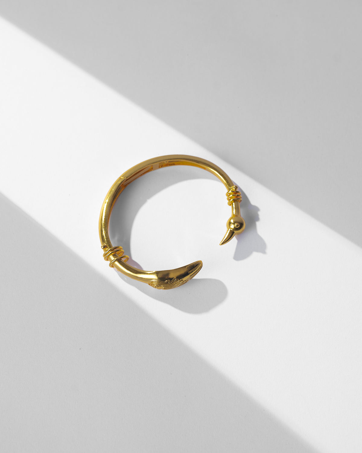 Gold Saras open cuff with a sculpted bird-head end.