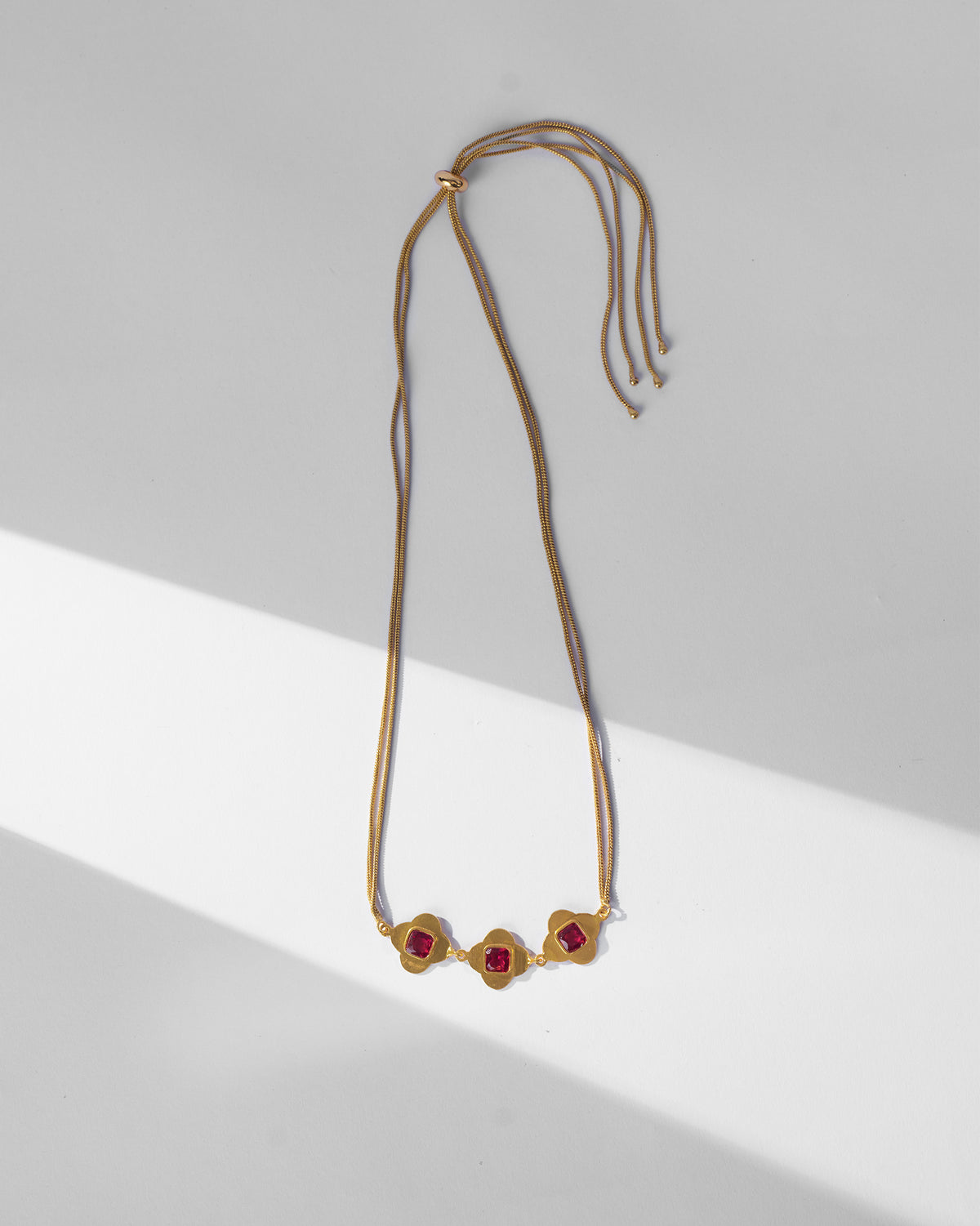Gold Ahiliya choker laid flat showing three pink glass motifs and slider.