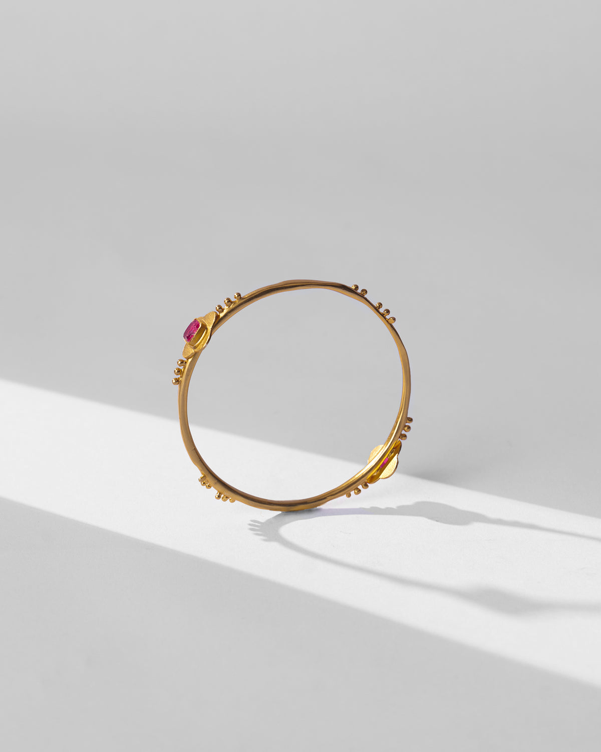 Gold Ahiliya bangle standing upright with pink glass accents.