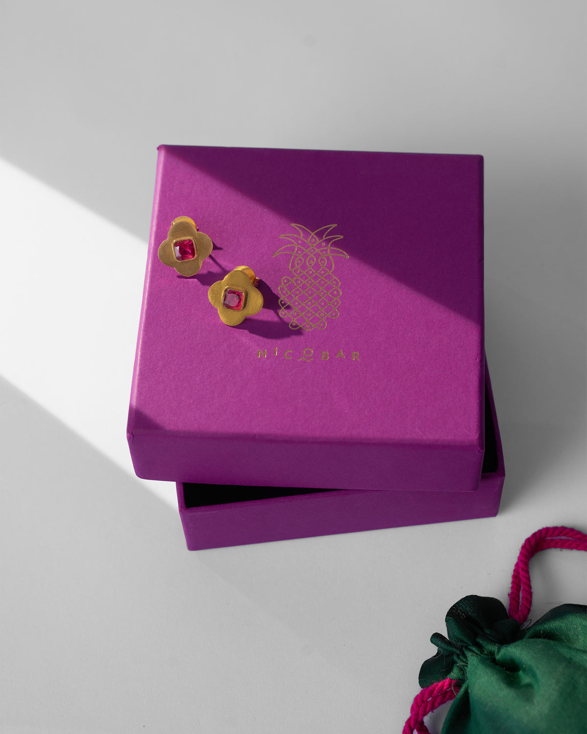 Gold Ahiliya studs with pink glass on a purple Nicobar gift box.