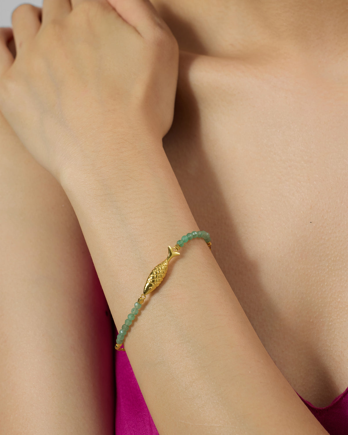 Gold Maase bracelet with green aventurine beads and a fish charm on a wrist.