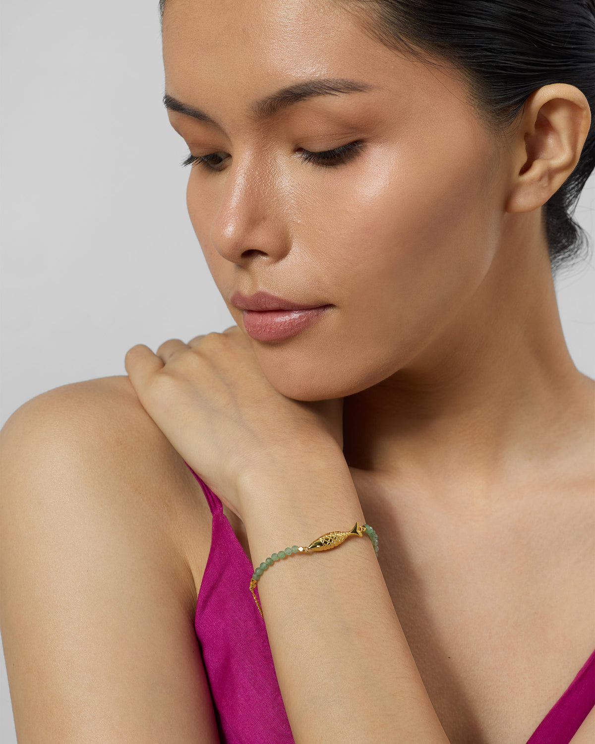 Person wearing a gold Maase bracelet with green beads and a fish charm.
