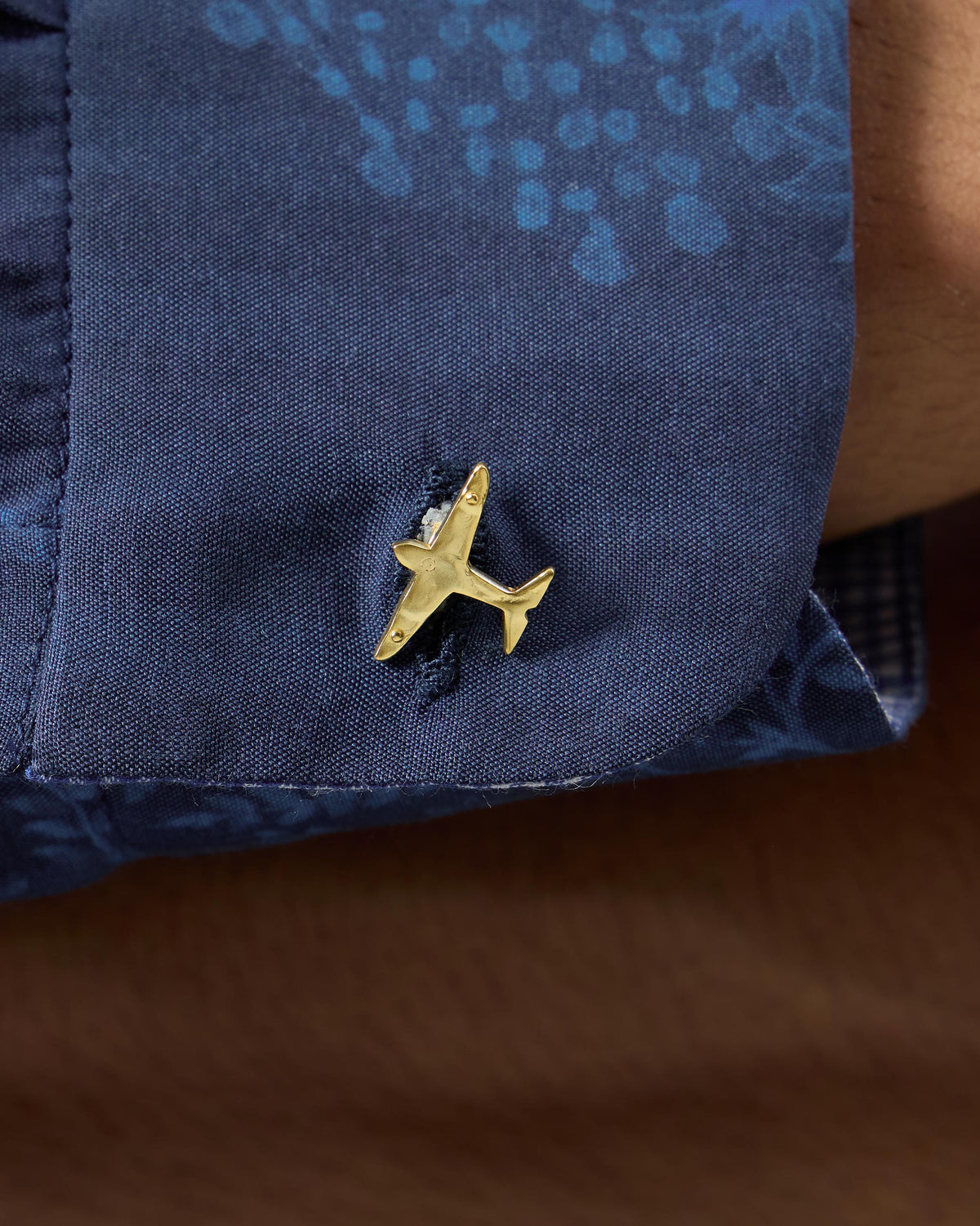 Close-up of a gold airplane cufflink on a navy shirt cuff.
