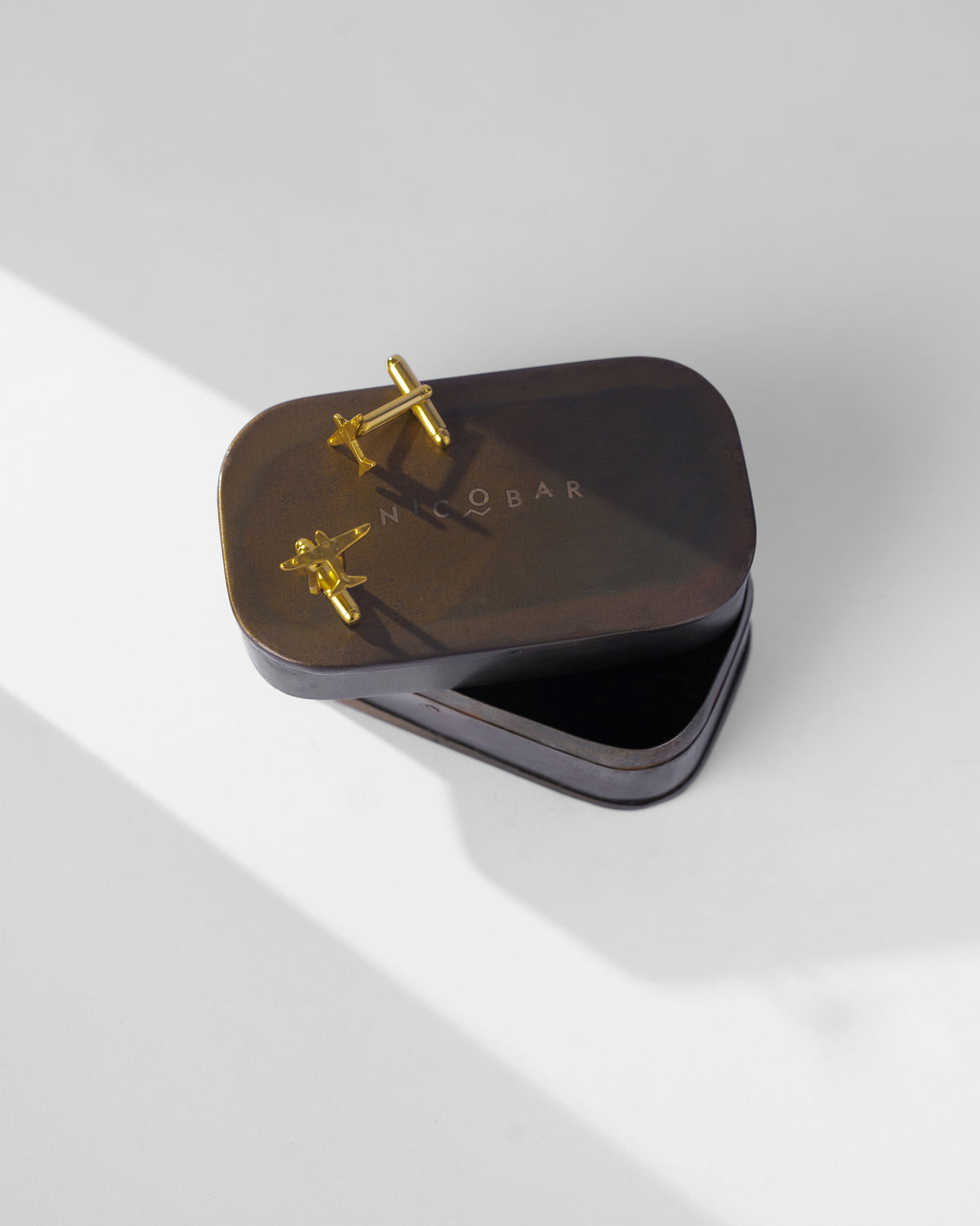 Pair of Flight Cufflinks resting on a dark brown tin lid.