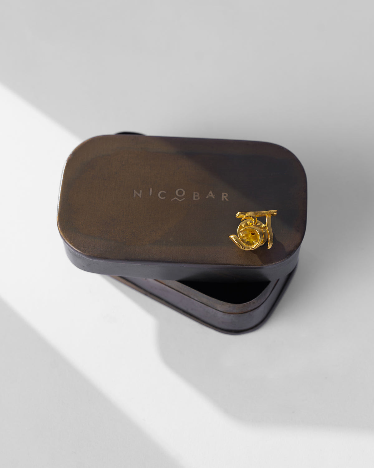 Gold Alphabet A Pin on the lid of a Nicobar tin.