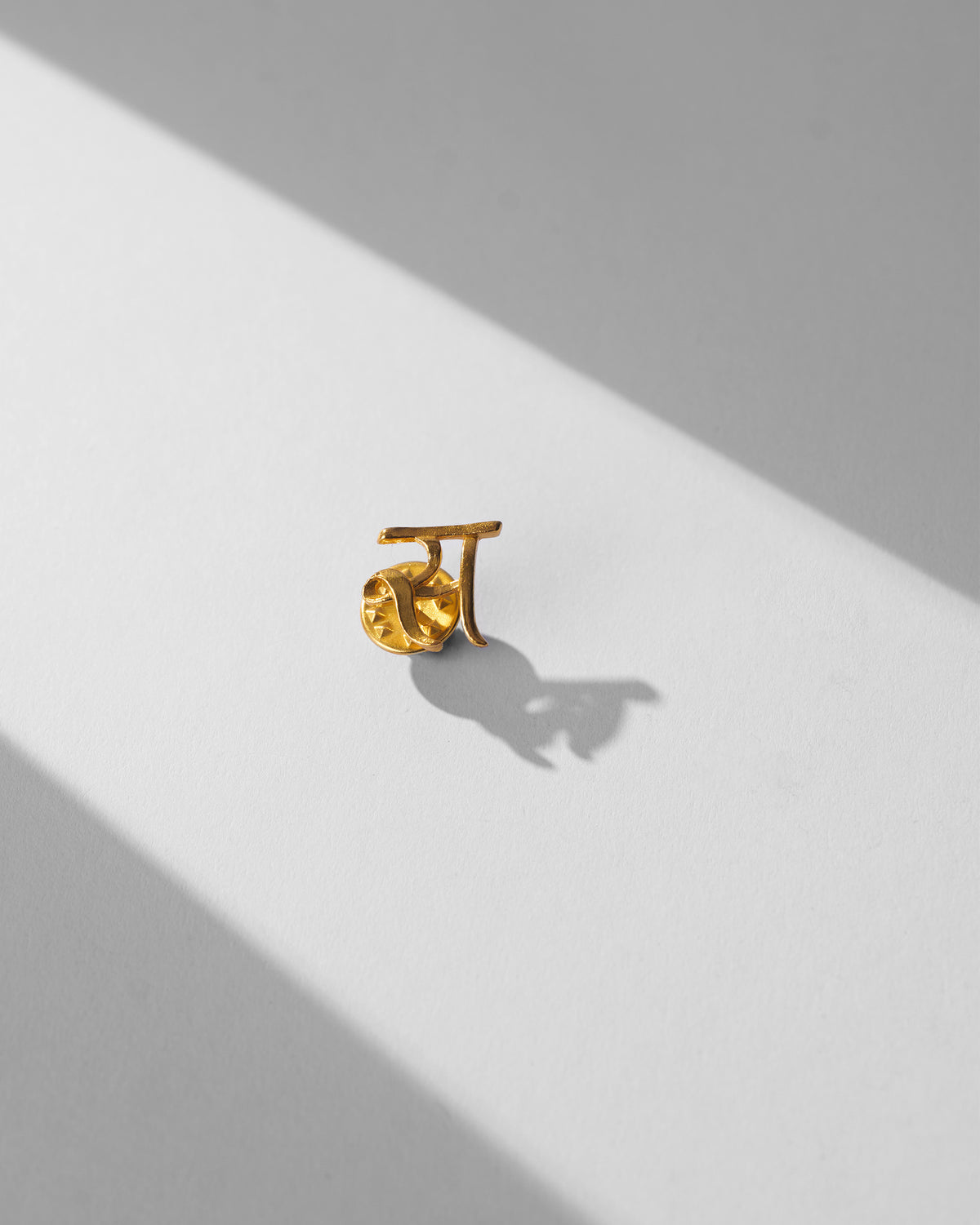 Close-up of gold Alphabet S Pin on a white surface.