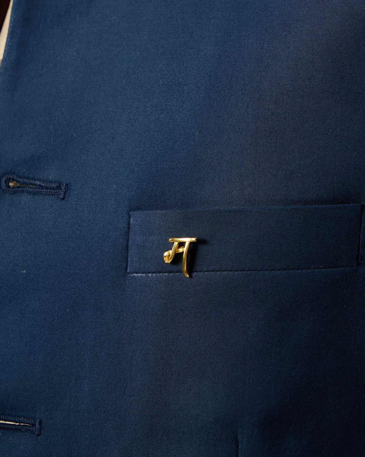 Close-up of Alphabet M Pin in gold on a navy pocket.