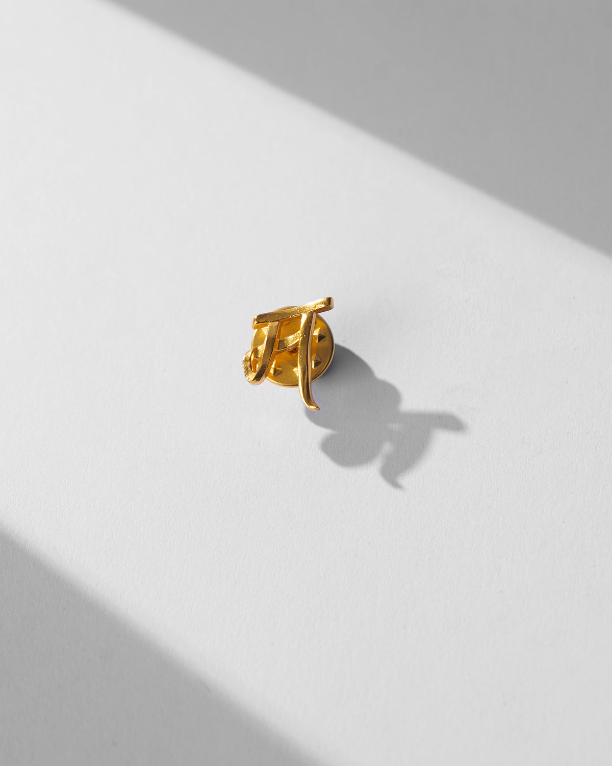 Alphabet M Pin in gold, shown alone in close-up.