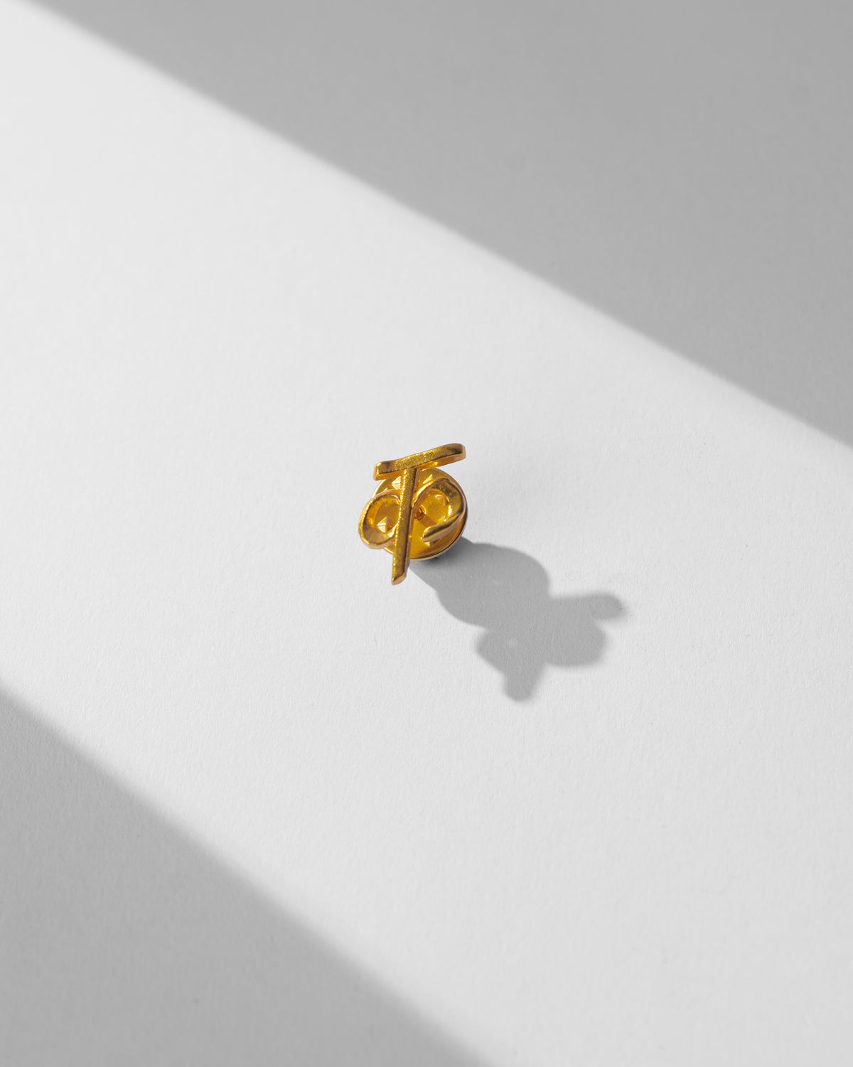 Close-up of gold Alphabet K Pin on a white surface.
