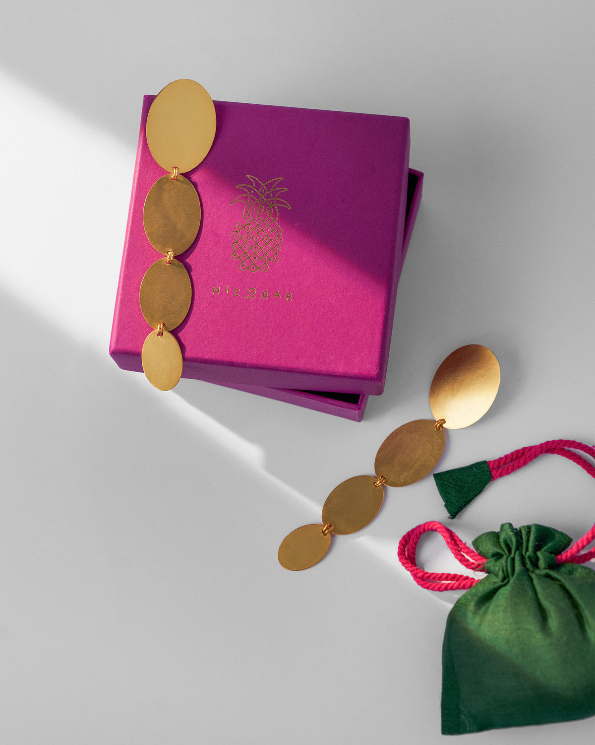 Pair of Drift Danglers arranged on a magenta gift box beside a green pouch.