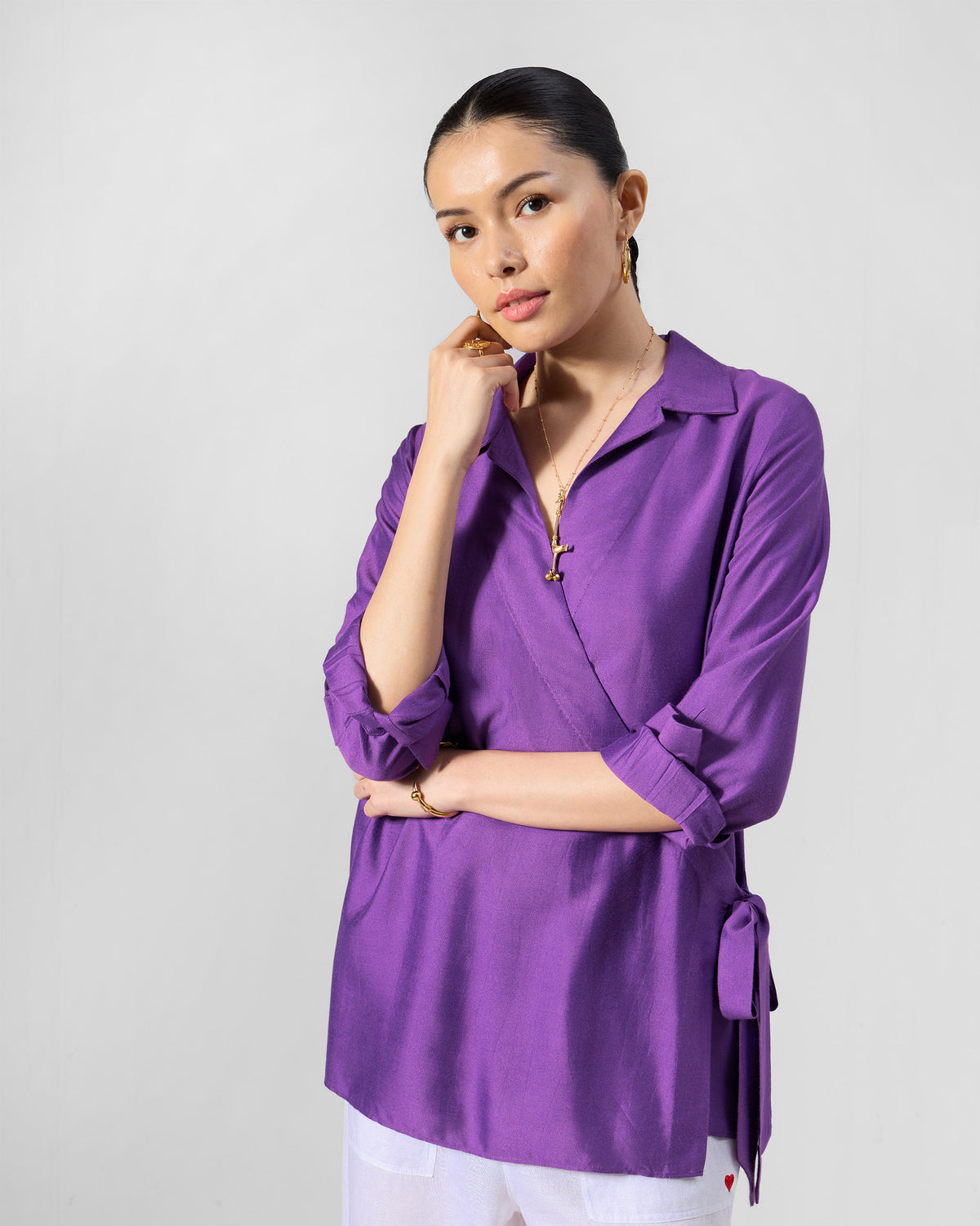 Person wearing a purple Katya shirt with a wrap front and side waist tie.