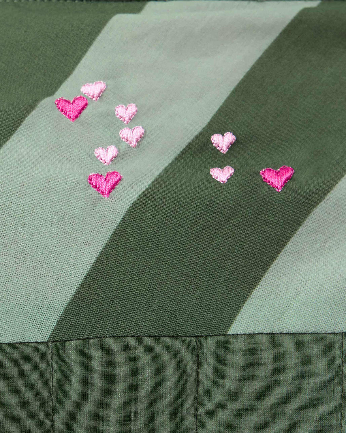 Close-up of pink heart embroidery on an olive striped Amalis shirt.