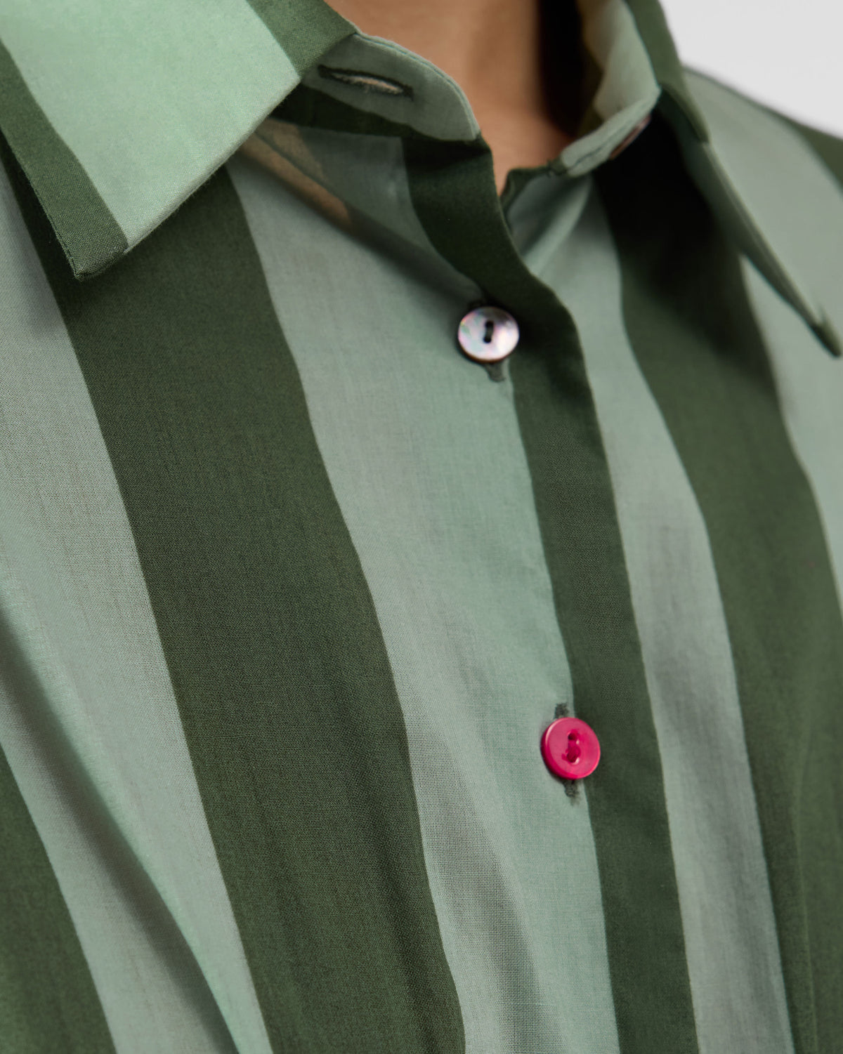 Close-up of an olive striped Amalis shirt collar with a pink button.