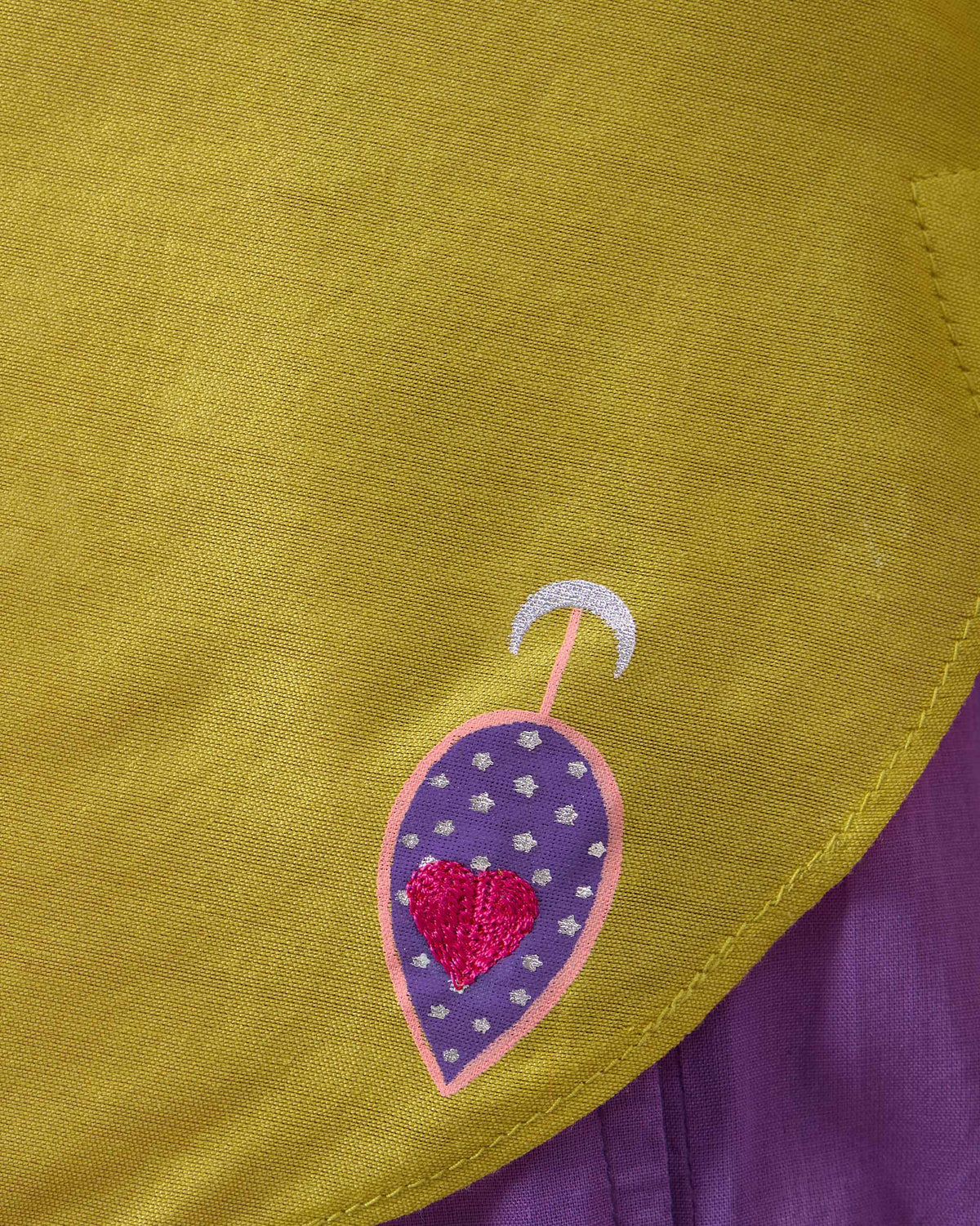 Close-up of a purple teardrop and pink heart on a chartreuse Chilika shirt hem.