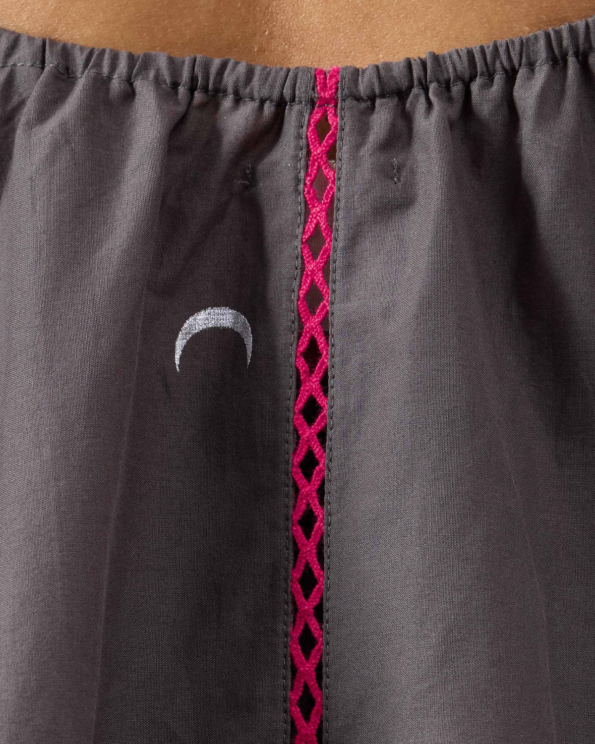Close-up of pink lattice stitching and a crescent on a charcoal Daman top.