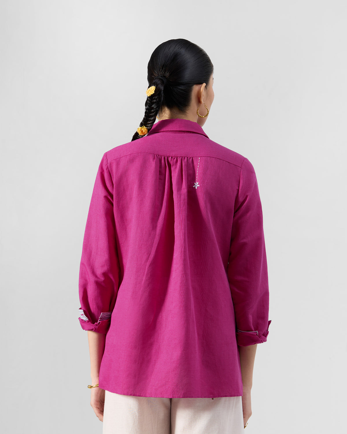 Back of a berry pink Mati shirt with a small white flower on the yoke.