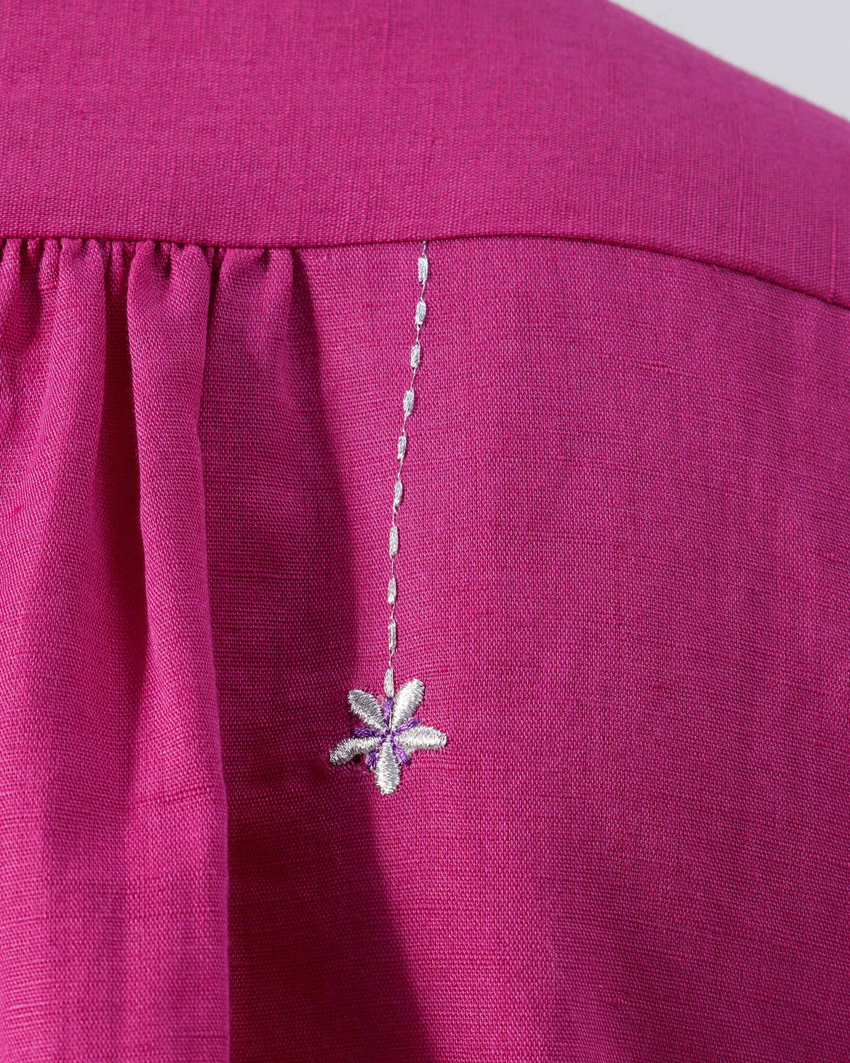 Close-up of a small embroidered flower on a berry pink Mati shirt yoke.