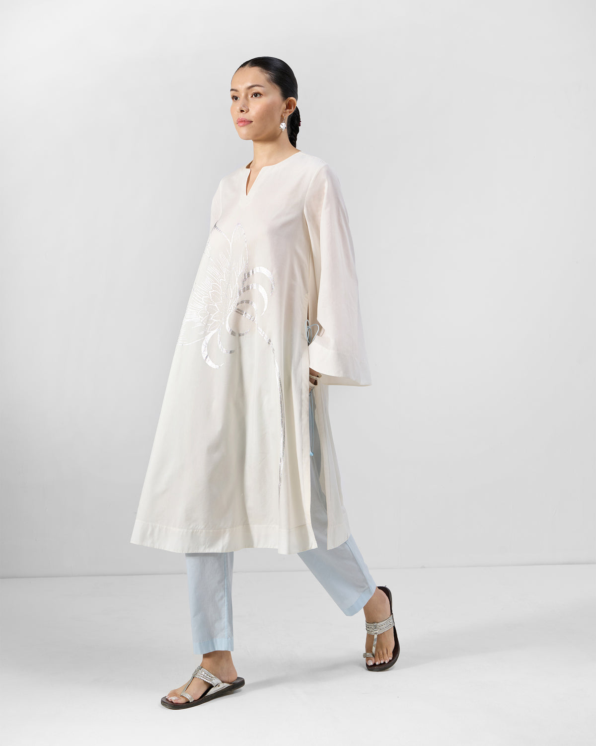 Person wearing an ivory Vaya kurta with a silver lotus foil print and flared sleeves.