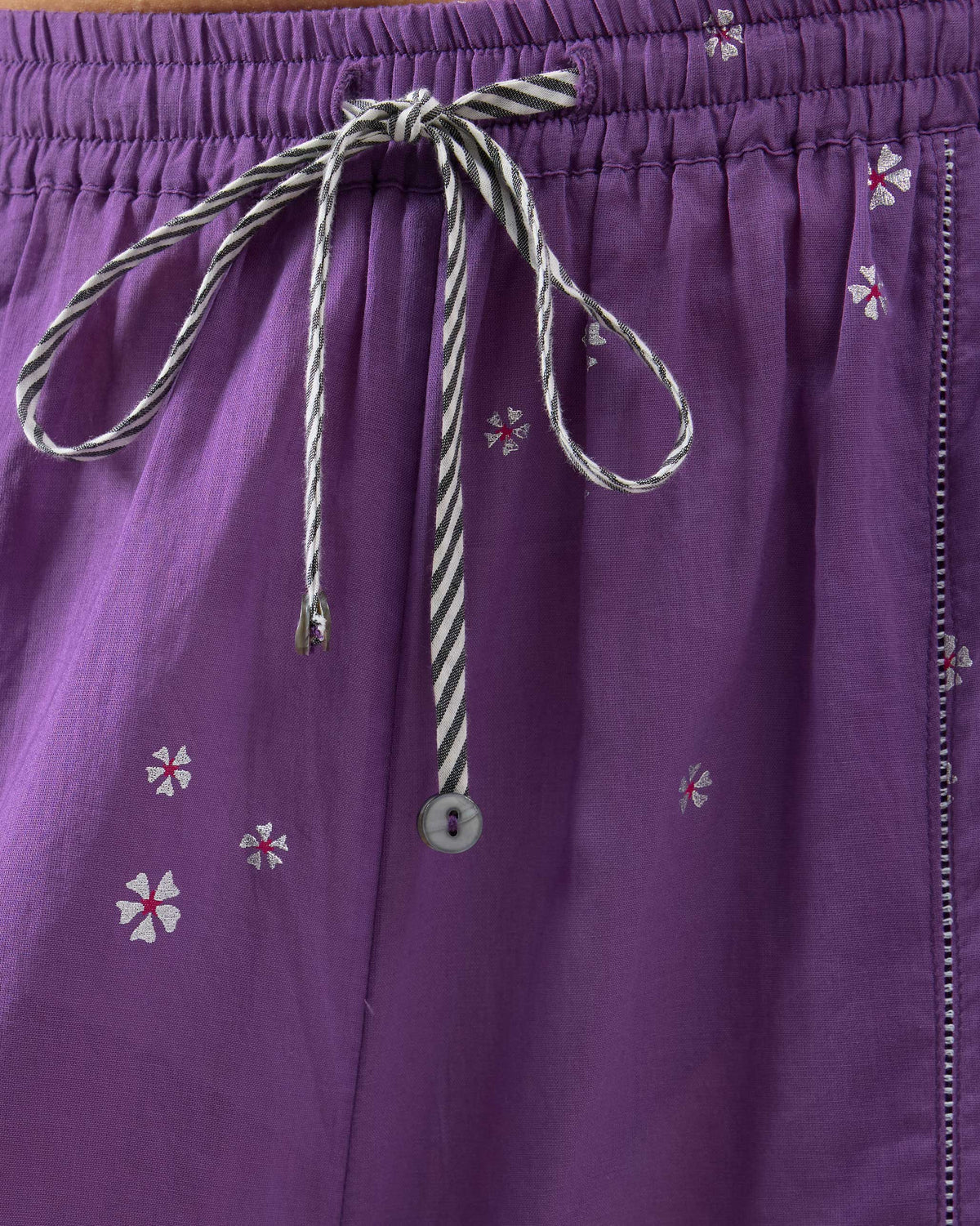 Close-up of the striped drawstring and white floral embroidery on purple Bora pants.