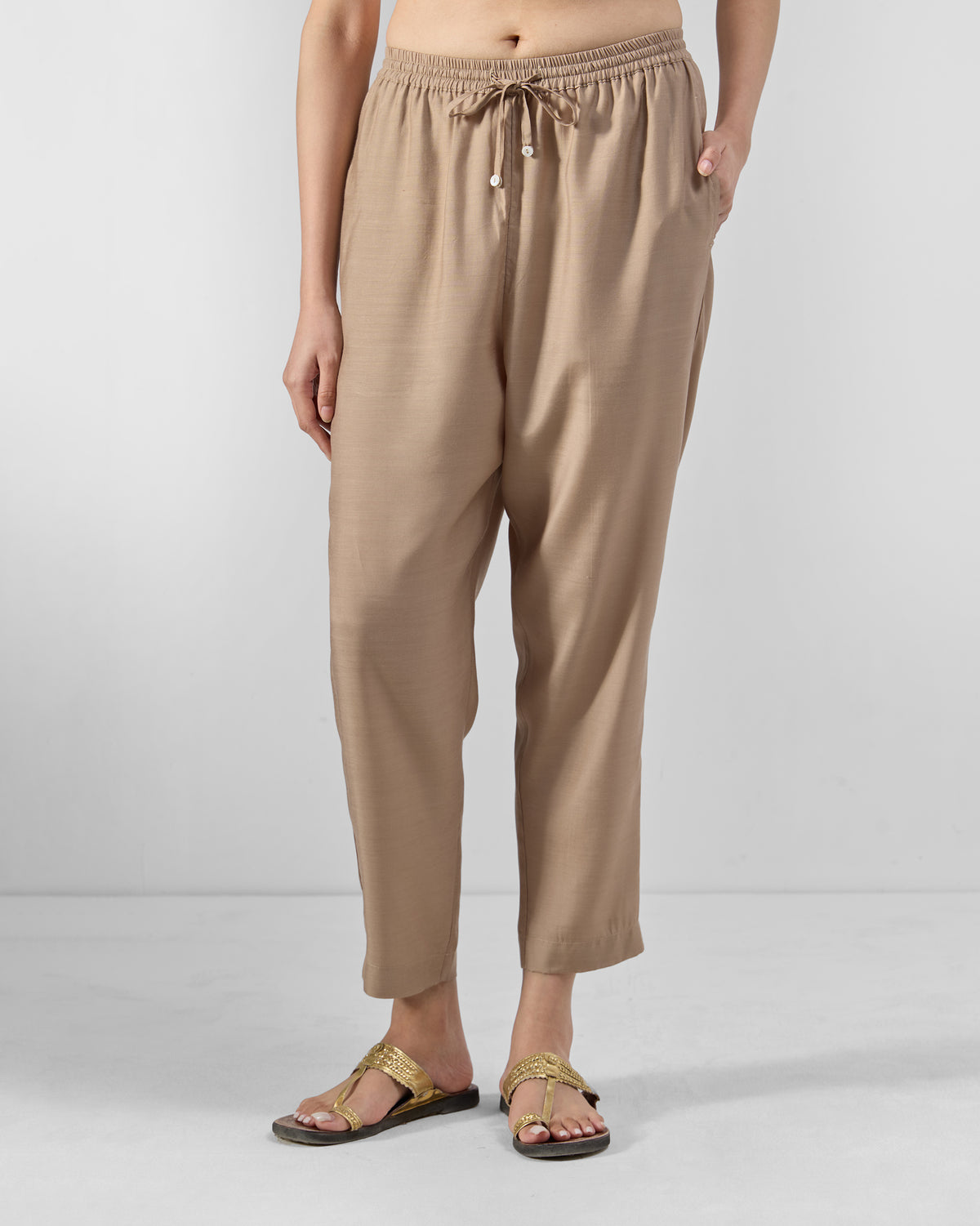 Person wearing sand Bemberg narrow pants with a drawstring waist.