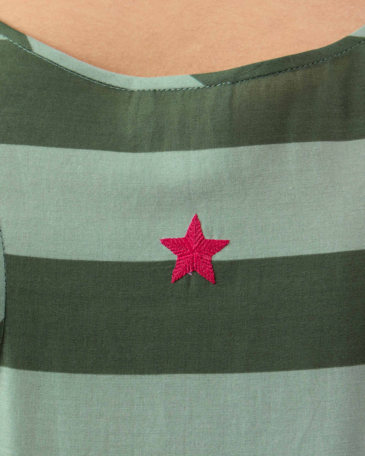 Close-up of a green Nora dress showing a pink embroidered star on the striped bodice.
