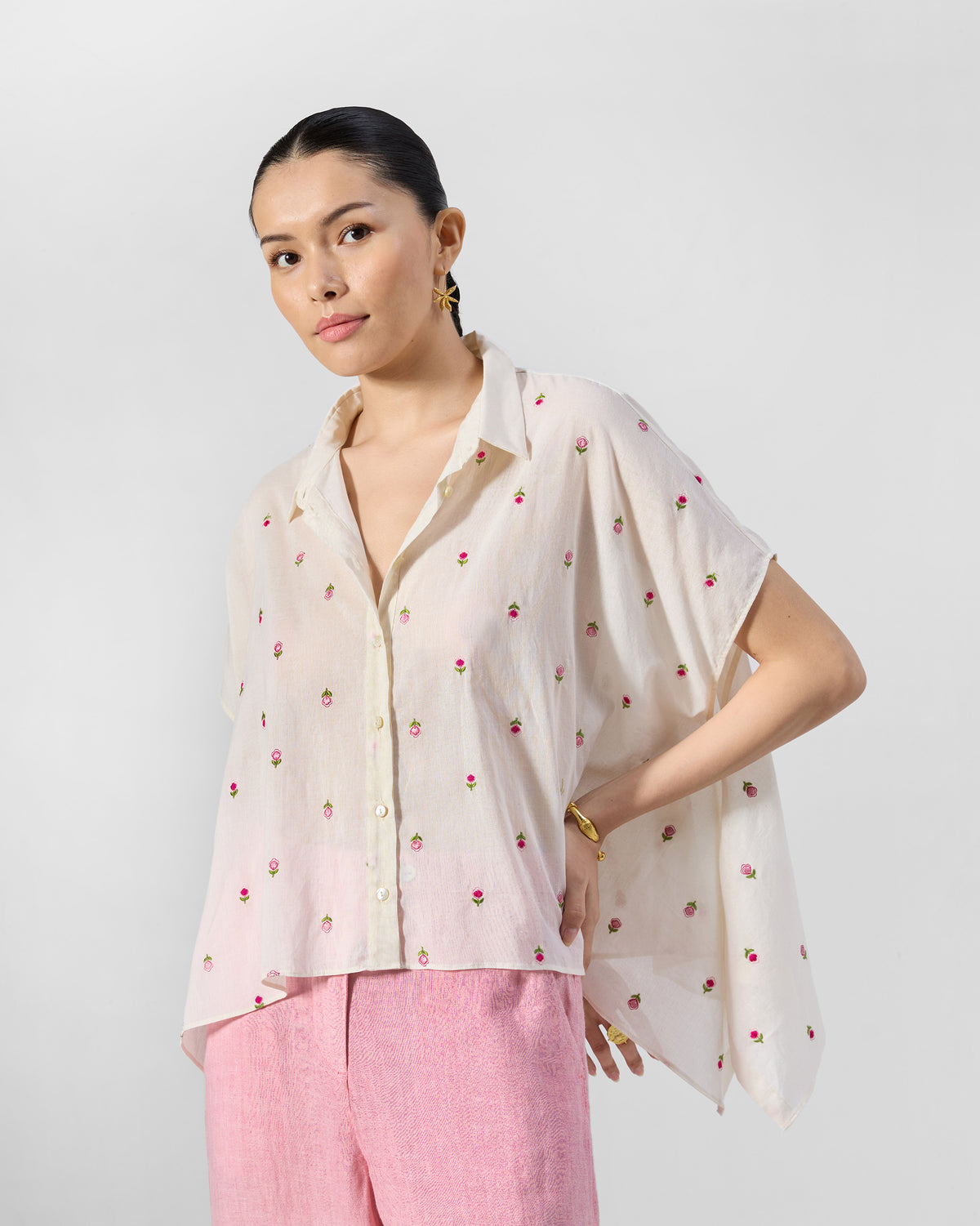 Person wearing an ivory loose cotton shirt with pink rose embroidery.