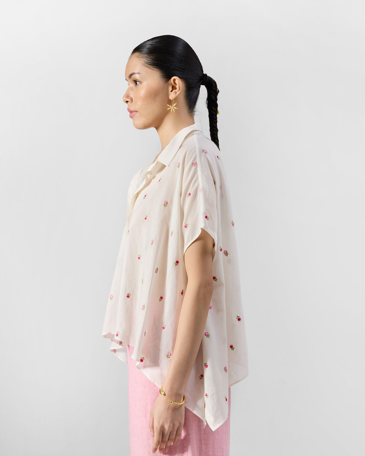 Side view of an ivory loose shirt with pink rose embroidery and a high-low hem.