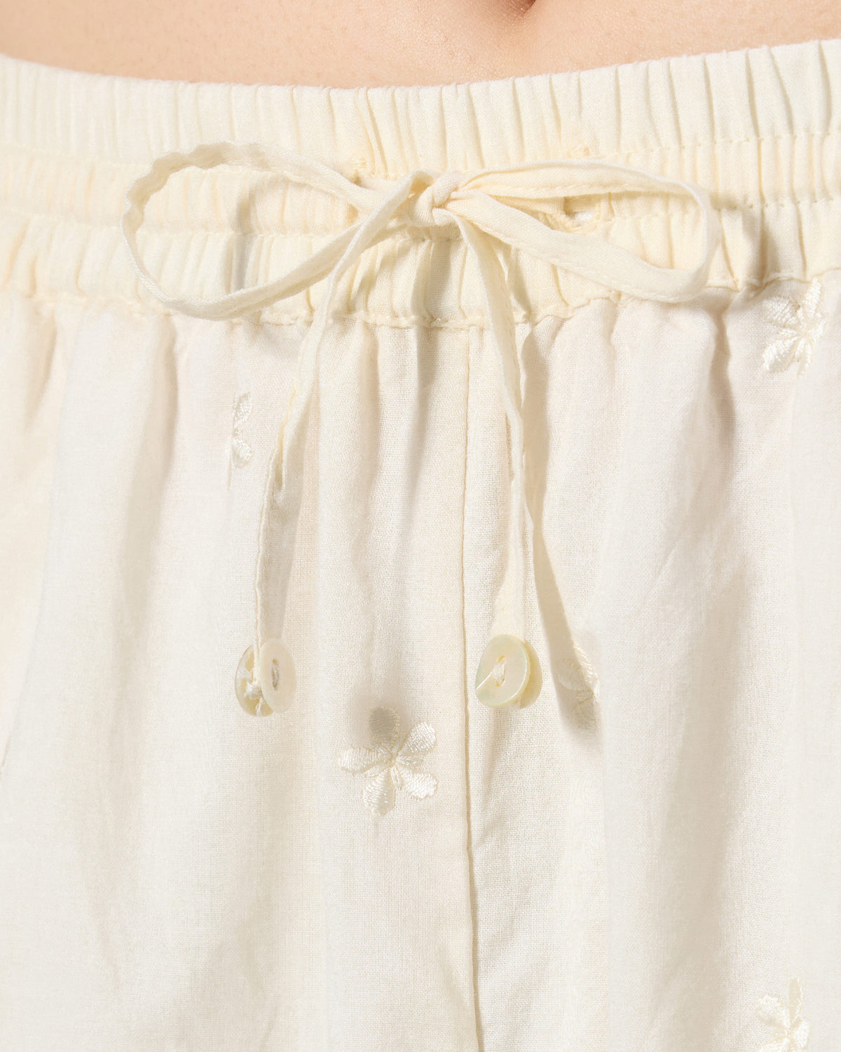 Close-up of an ivory drawstring with button ends on embroidered Kintara Pants.