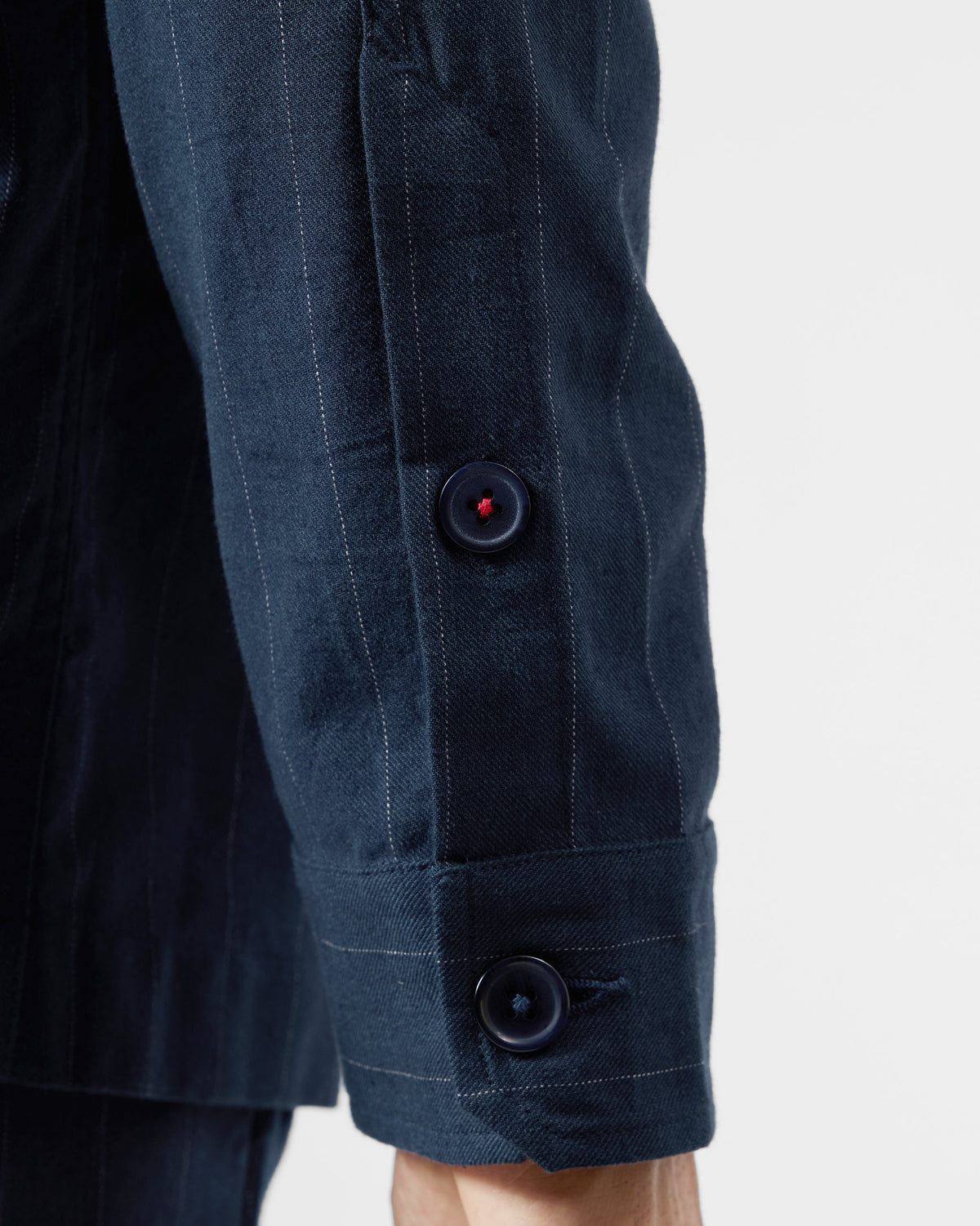 Close-up of a navy pinstripe Rayh shacket cuff with a red-stitched button.