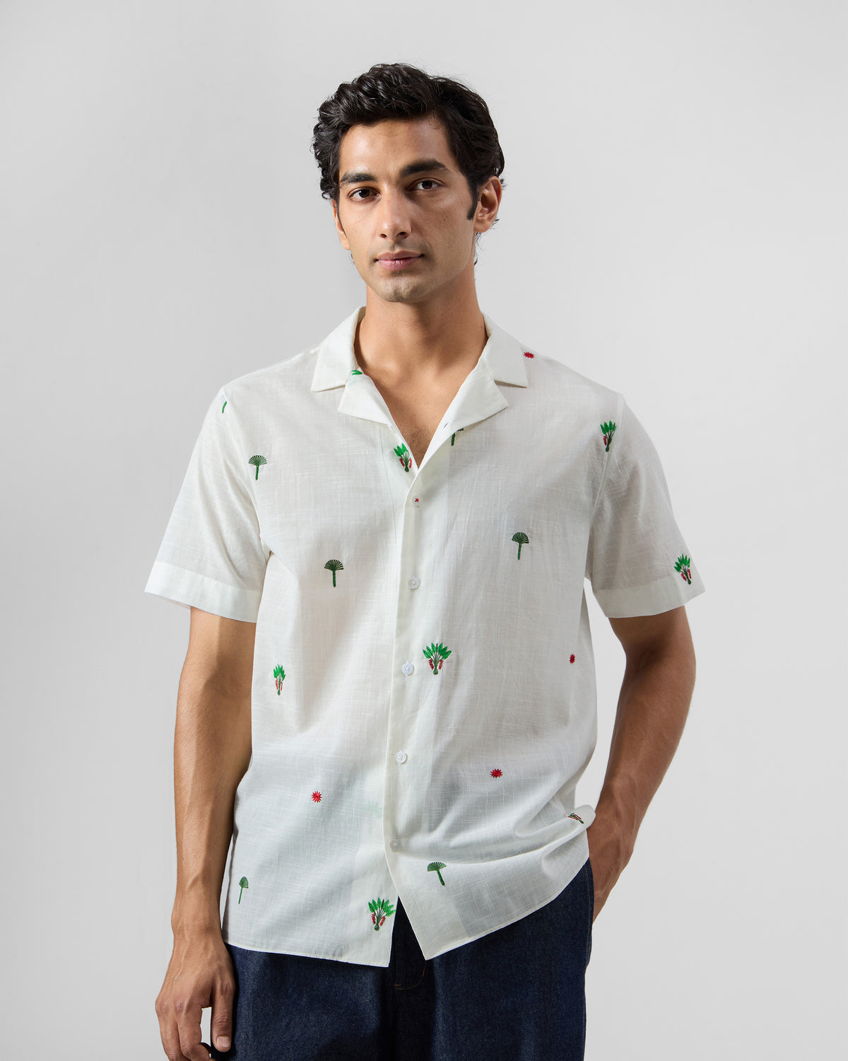 Person wearing a white Delta Shirt with green palm embroidery and a camp collar.