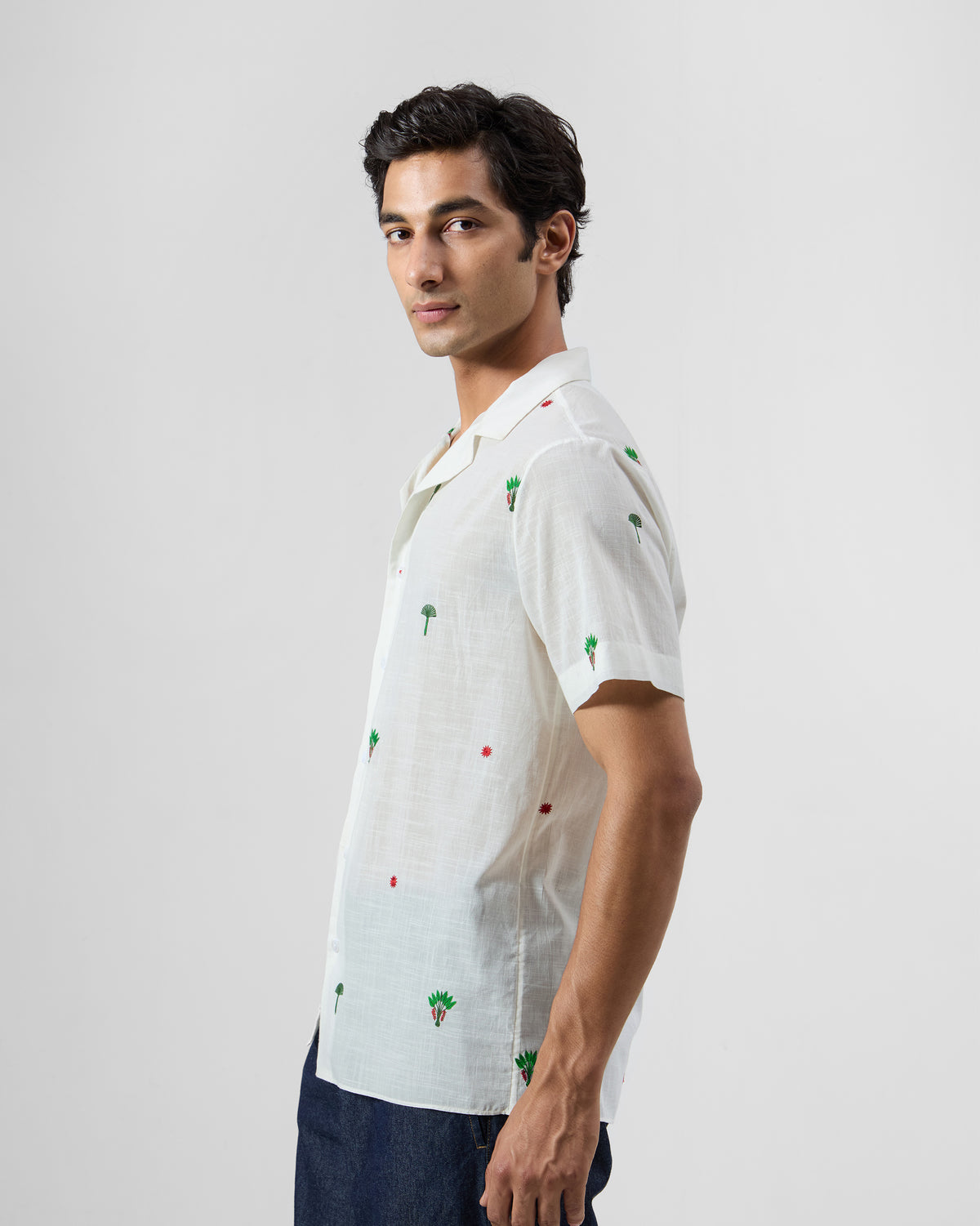 Side view of a white Delta Shirt with green palm embroidery tucked into trousers.
